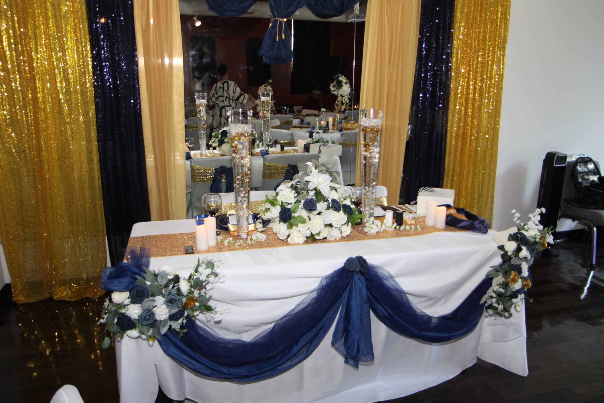 Head table decorated with navy drapery, gold sequins and white florals