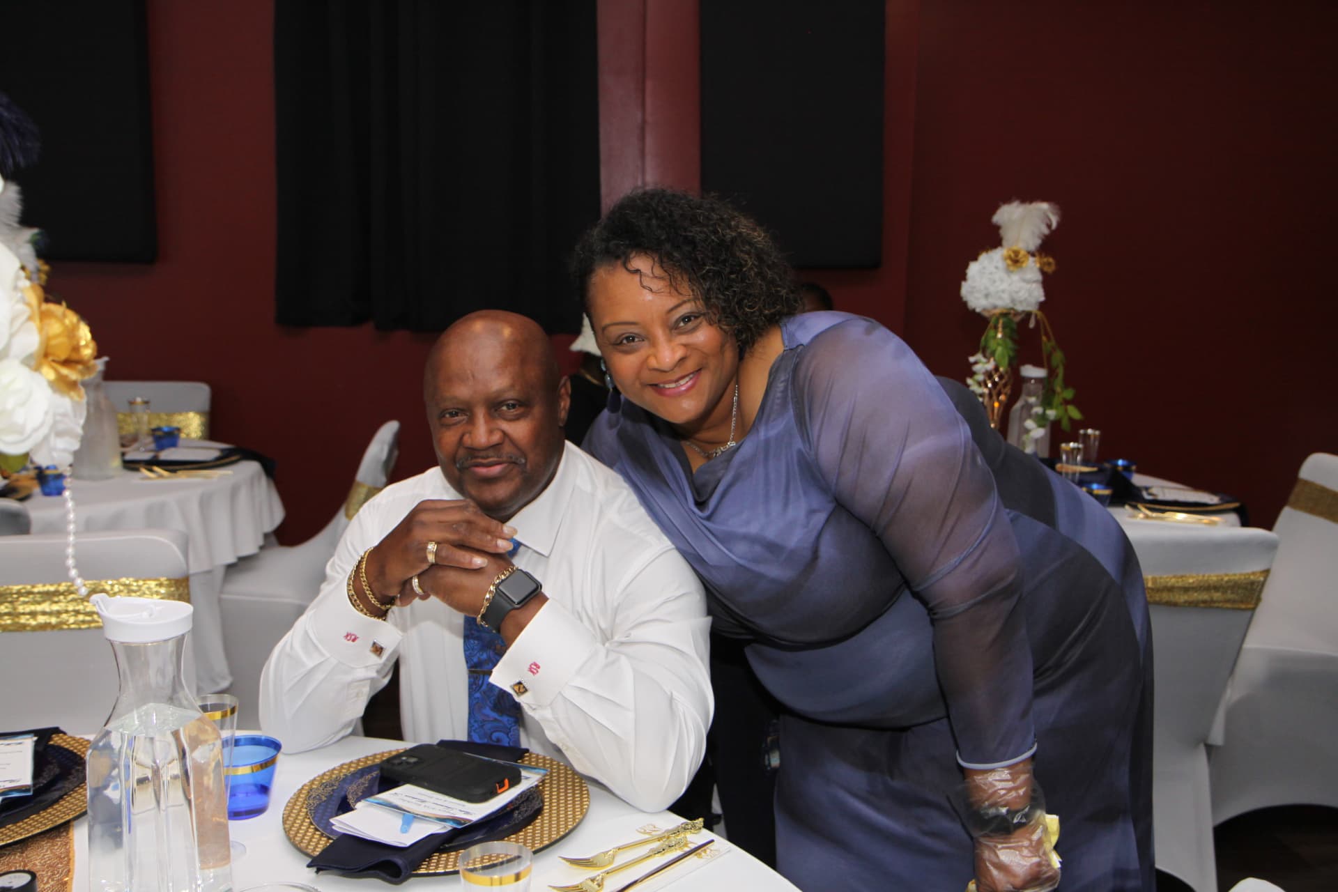 Pastor Lo seated at his table with a guest smiling beside him
