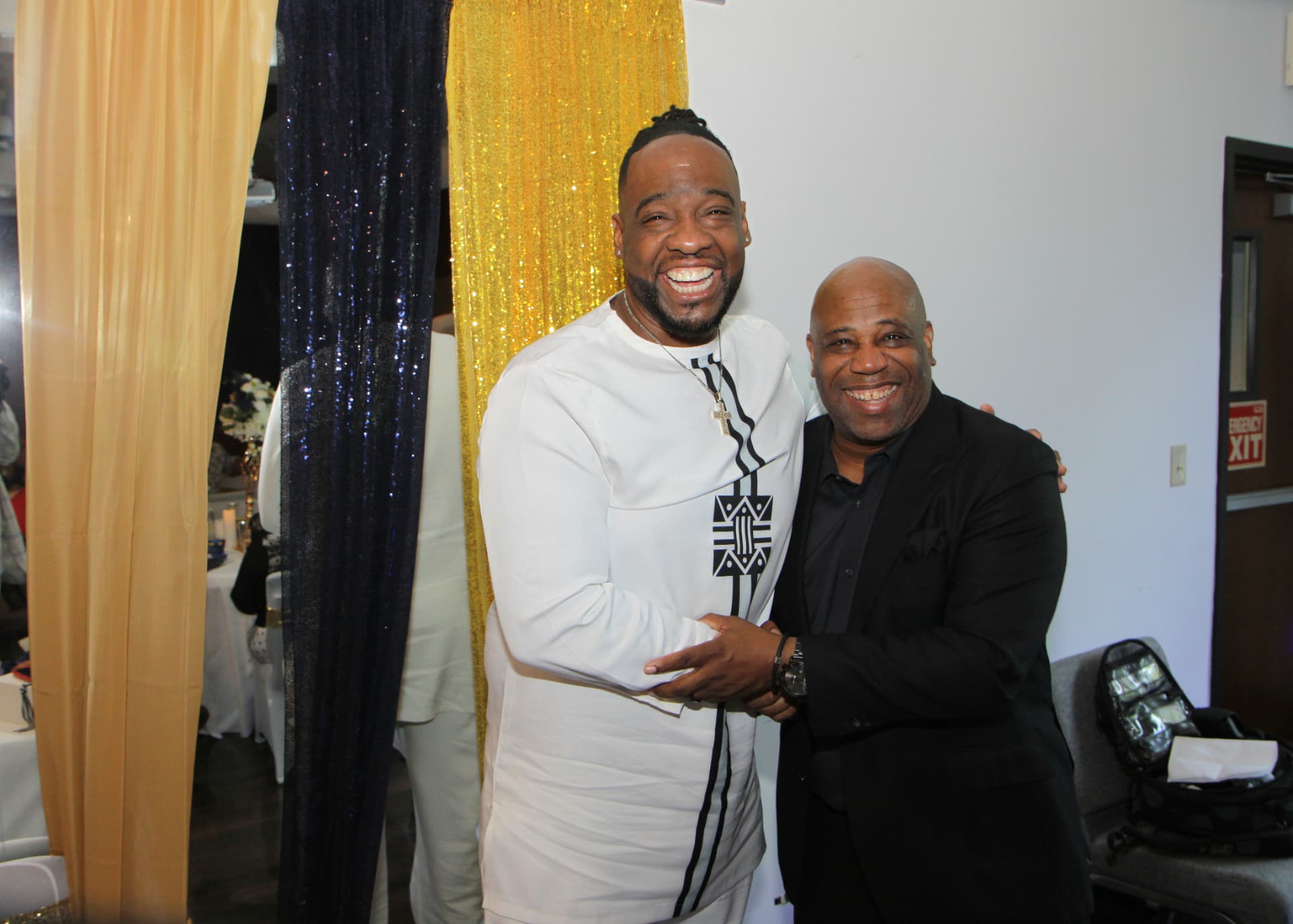 Pastor Lo embracing a guest in front of navy and gold drapery